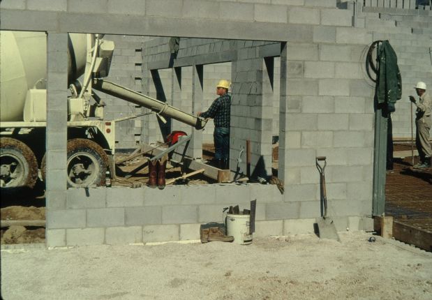 Men pouring a reinforced concrete floor on corrugated metal on top of steel trusses.