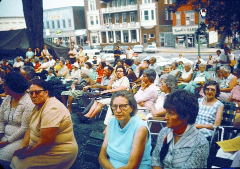 People seated in folding chairs on the town square.