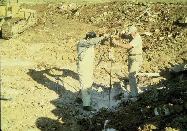 Two men drilling a hole to place explosives.
