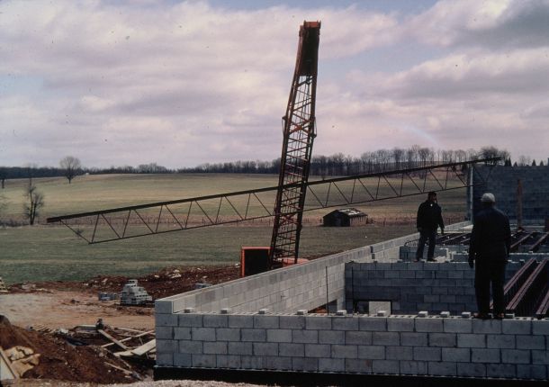 Men walking on top of concrete block walls, placing structural steel for the floor above.