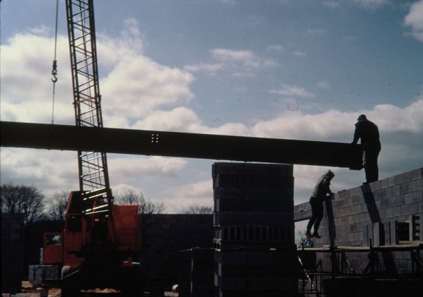 Crane and men installing a large structural steel beam.