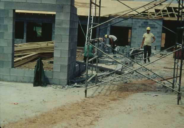 Men building a concrete block wall beyond scaffolding.