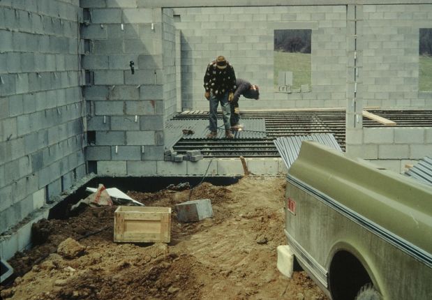 Men placing corrugated steel decking on steel trusses before pouring a concrete floor.
