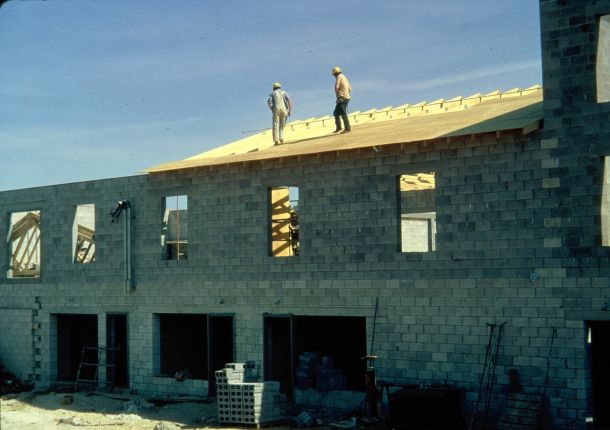 Wooden trusses and roof being installed on two-story concrete block structure.