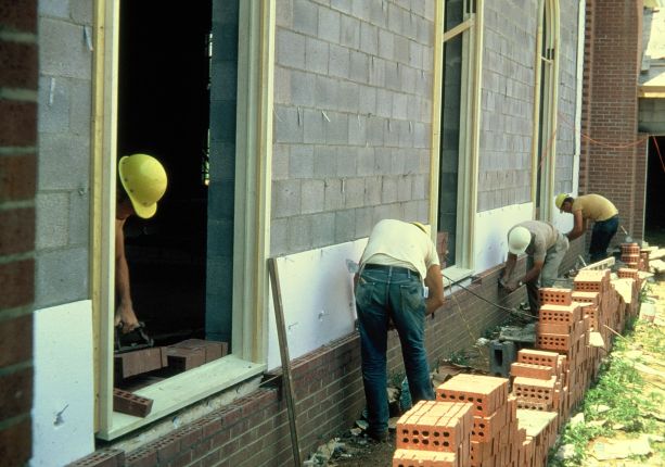 Men laying brick on exterior wall of a church.