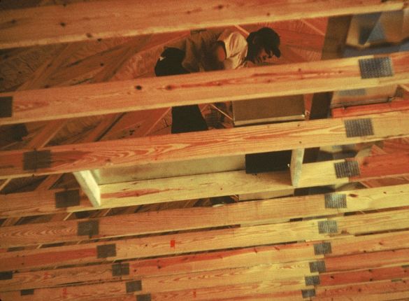 Men installing ventilation ductwork through wooden trusses.