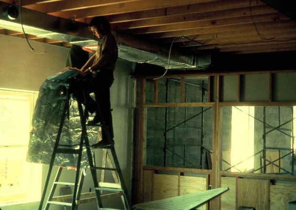 Man on a ladder installing ventilation ductwork.